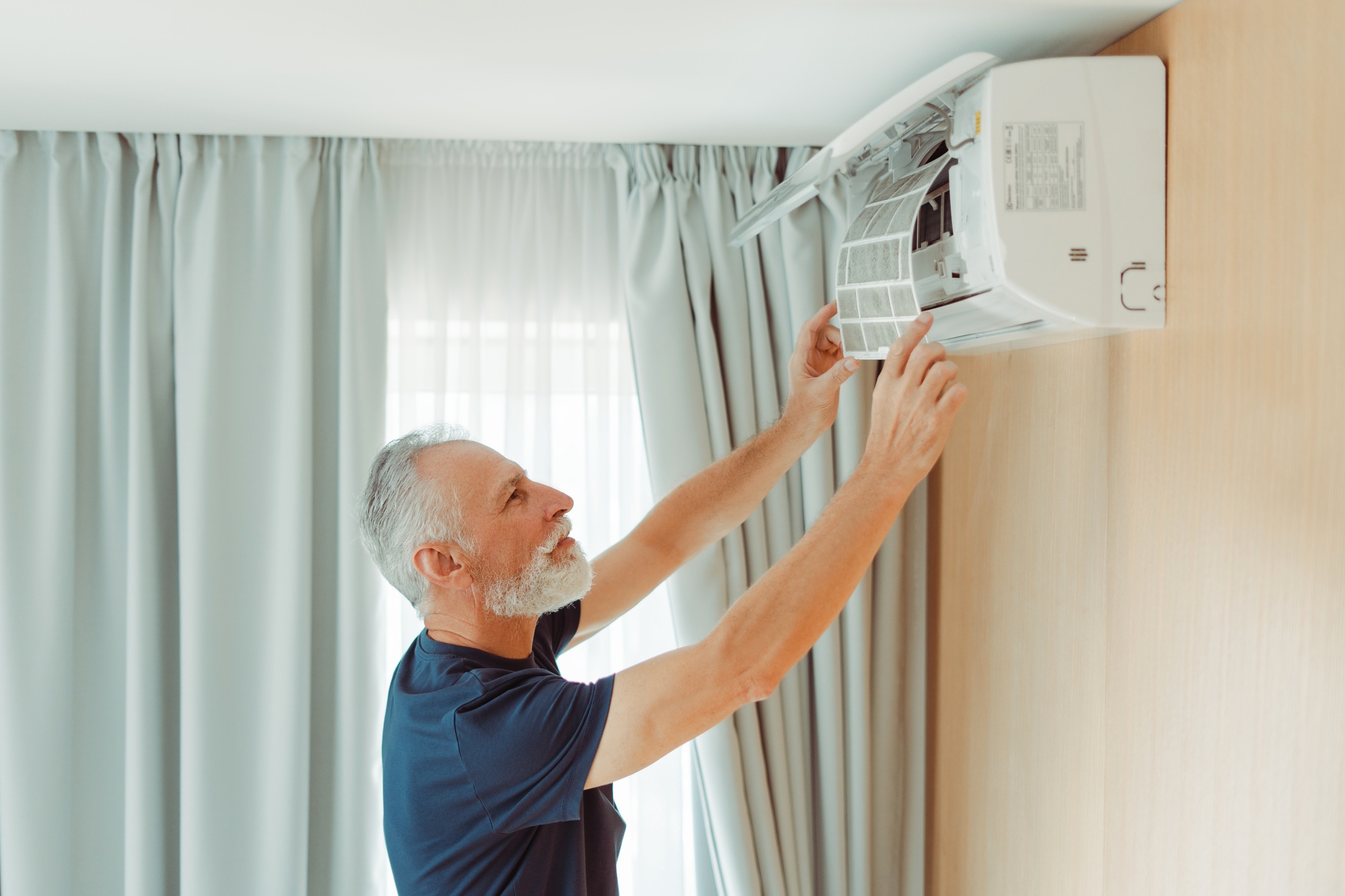 Attractive senior serviceman checking air conditioner cleaning air conditioner filter in apartment