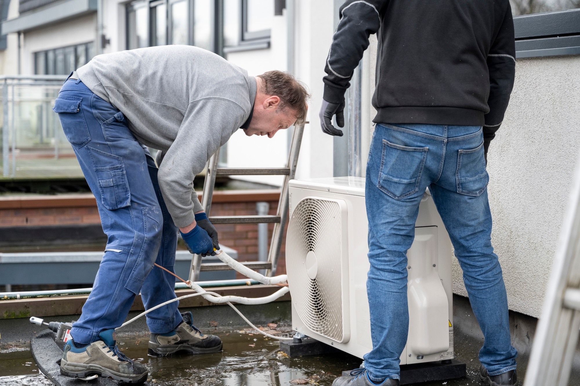 Two technicians installing an airconditioning unit outside a modern home.